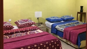 A room with two beds, each with patterned bedding and a nightstand with a lamp. A painting of a landscape hangs on the wall. - Bohok Guest House (Langkawi)