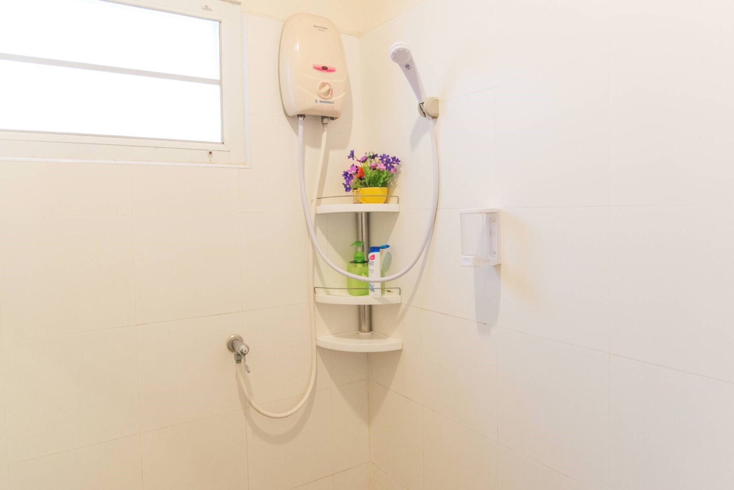 Un baño con ducha, secamanos y estante con artículos de aseo.