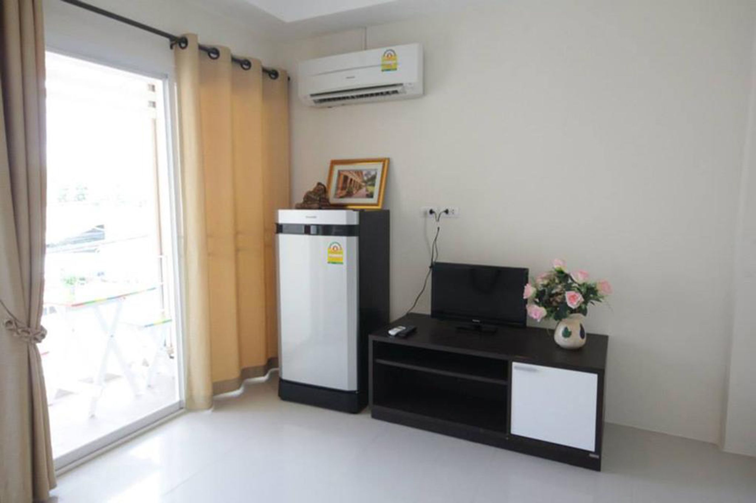 A modern room with a sliding glass door, a black TV stand, a refrigerator, and an air conditioning unit.