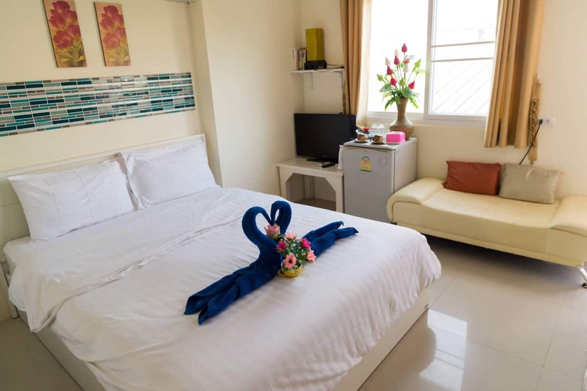 Een hotelkamer met een net opgemaakt bed, een klein bureau met een televisie, een bank en een raam met gordijnen.