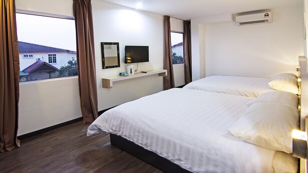 A hotel room with a large bed, a mounted TV, a small shelf with items, and a window with curtains. - Thanks Hotel (Nibong Tebal)