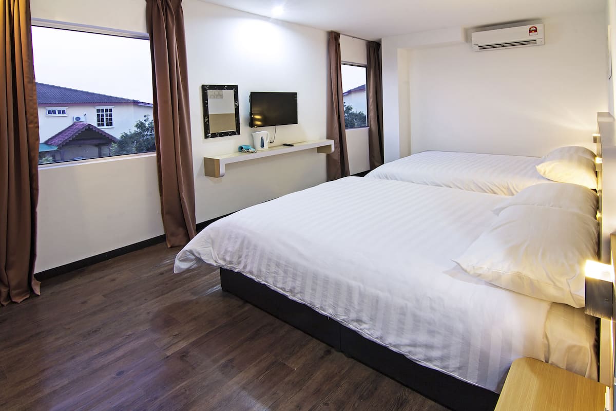 A hotel room with a large bed, a mounted TV, a small shelf with items, and a window with curtains.