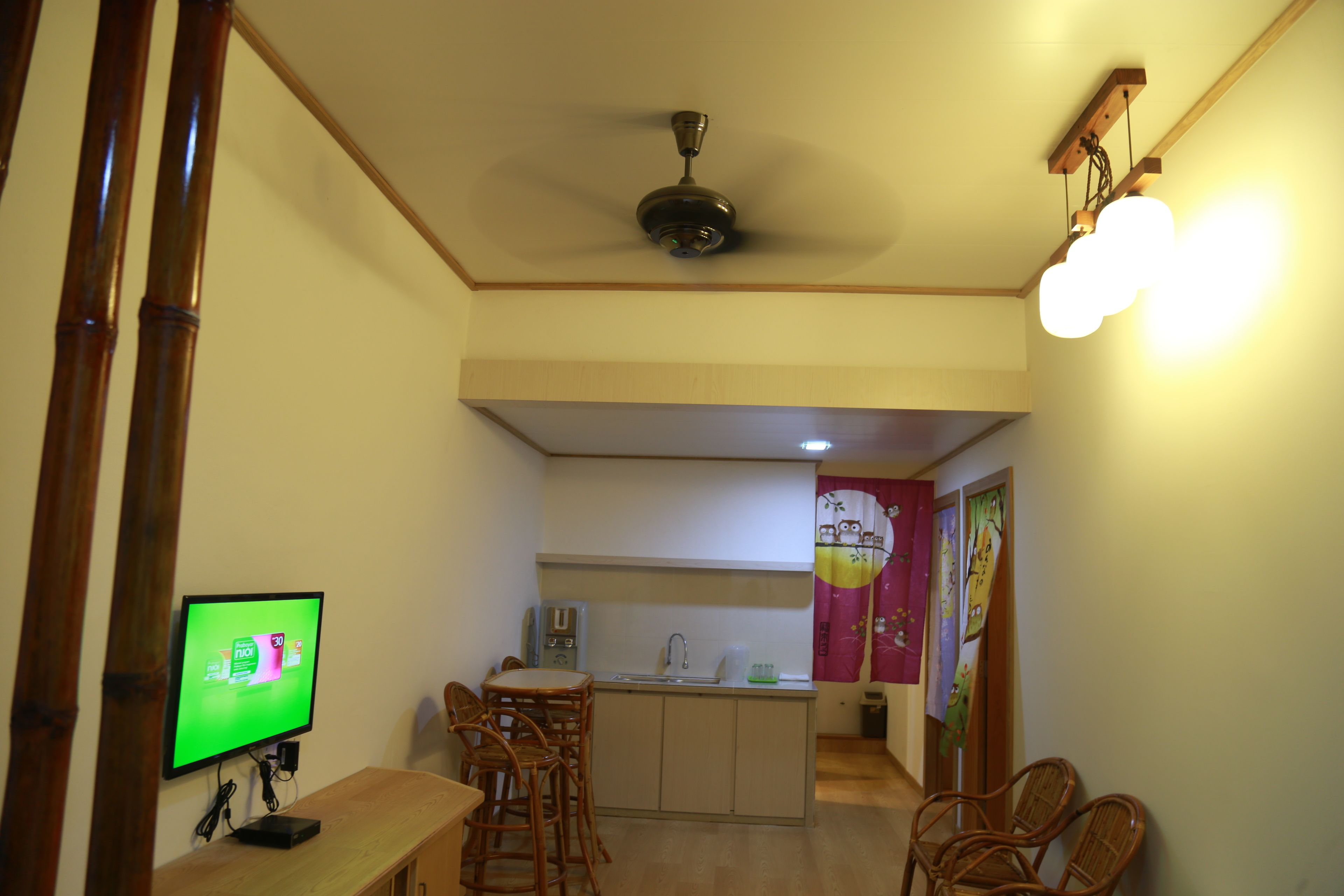 A compact kitchen with a dining area, a ceiling fan, a TV, and a small island with a sink.