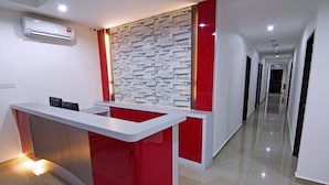 A reception desk with a red and white color scheme, a stone-textured wall, and a long hallway with doors. - Thanks Hotel (Nibong Tebal)