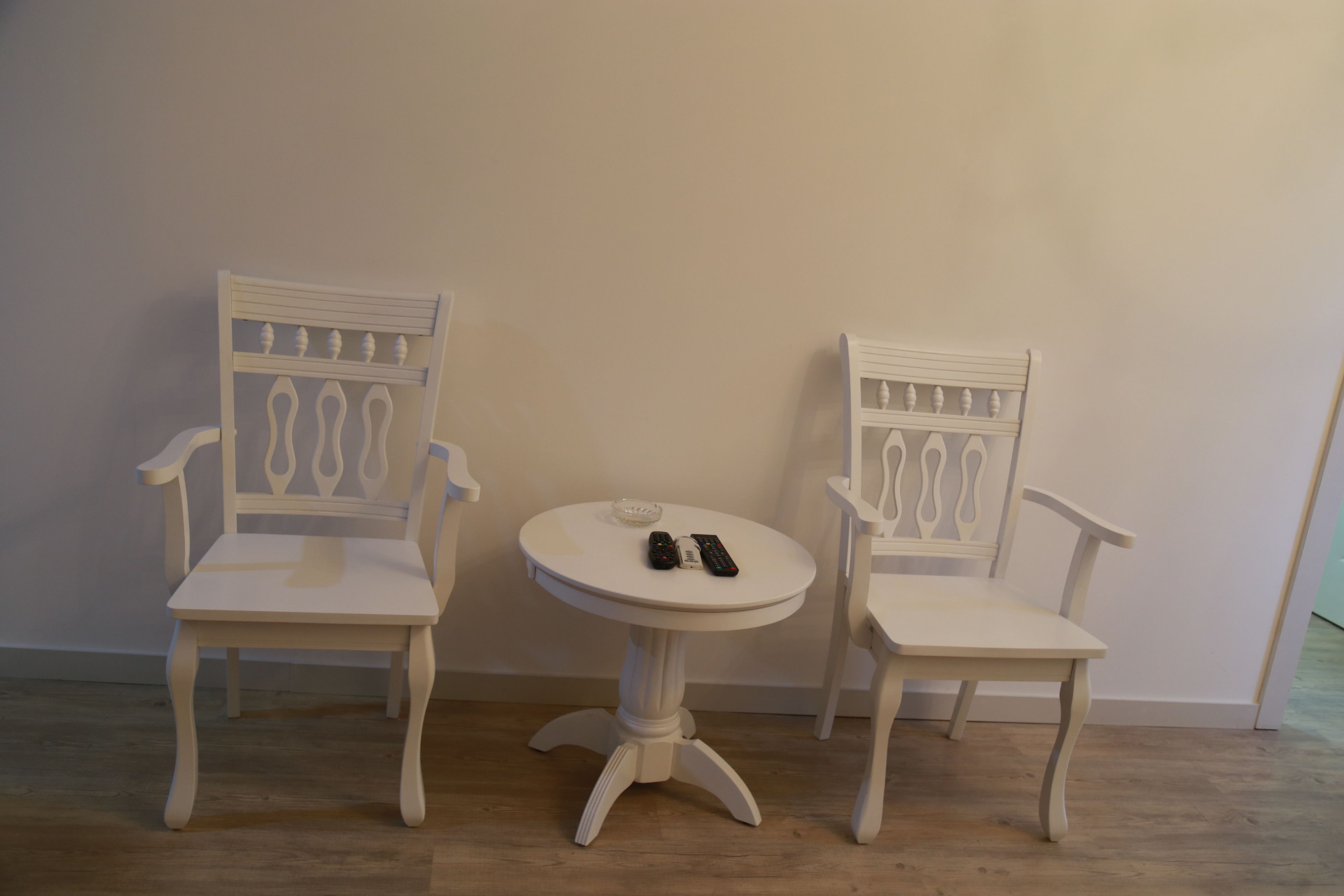 Two white chairs with a small round table between them, each with a remote control on the table.