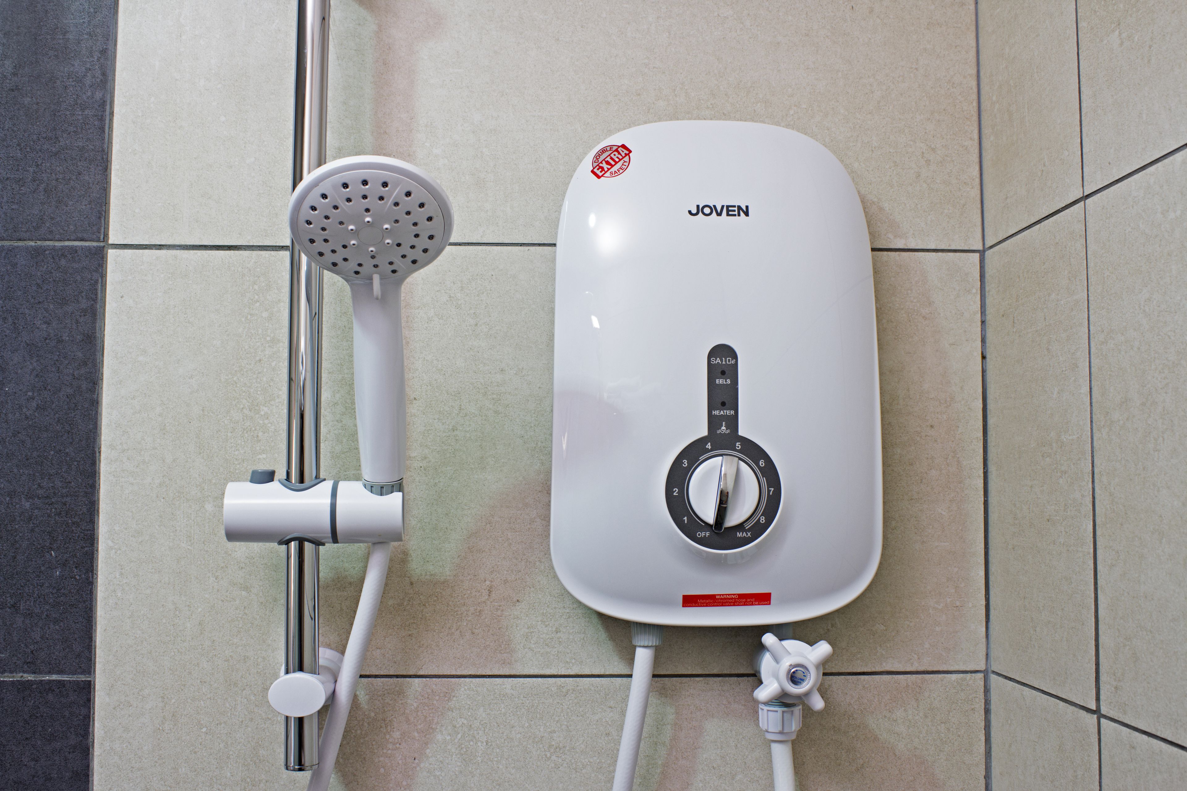 Calentador de agua Joven con un dial de control y un cabezal de ducha conectado a una tubería fijada a la pared.