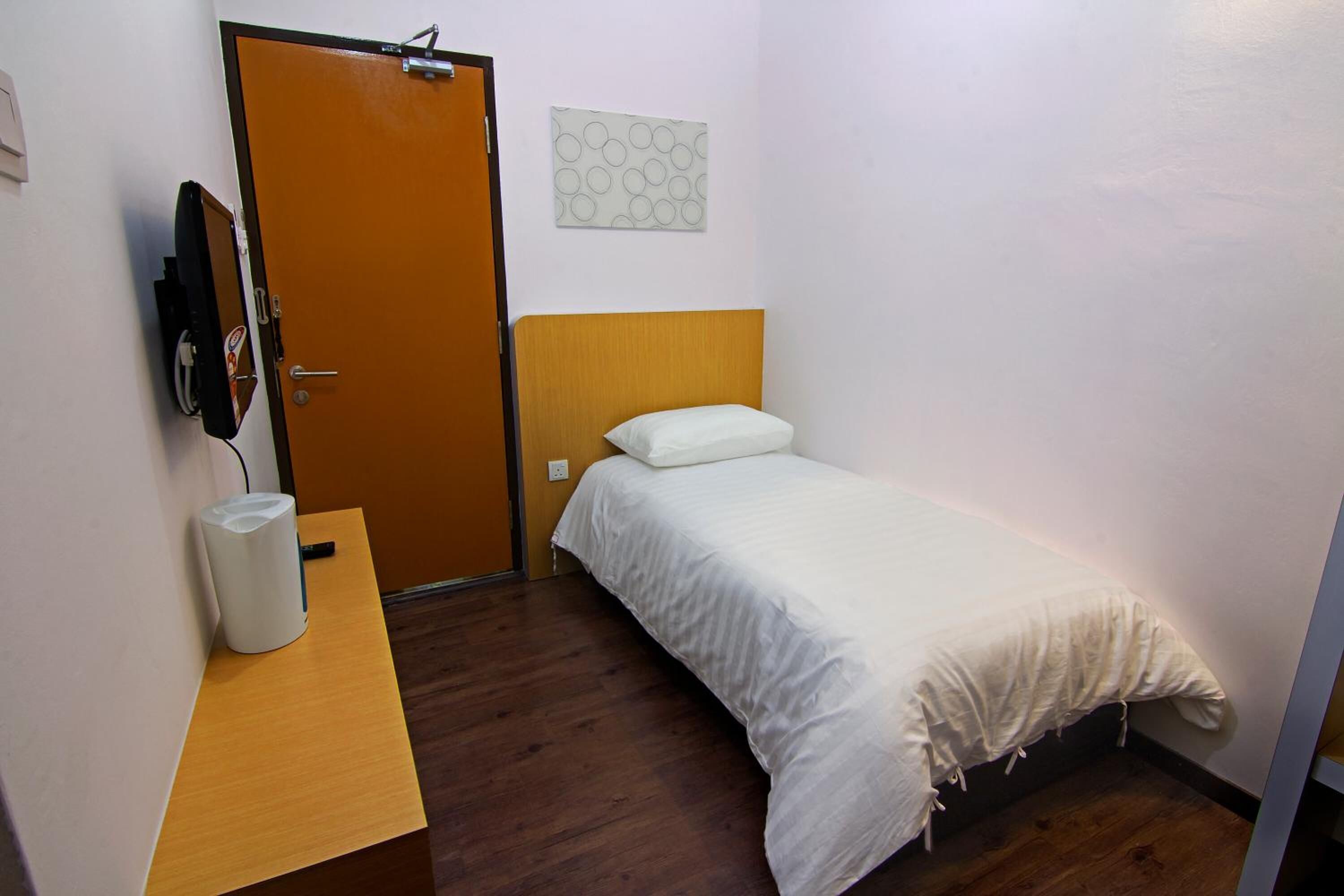 A small, neatly arranged room with a wooden bed, a bedside table with a lamp, and a door with a towel hanging on it.