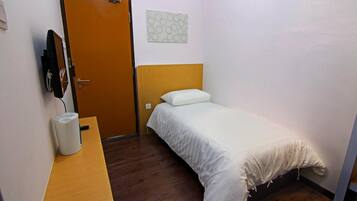 A small, neatly arranged room with a wooden bed, a bedside table with a lamp, and a door with a towel hanging on it.