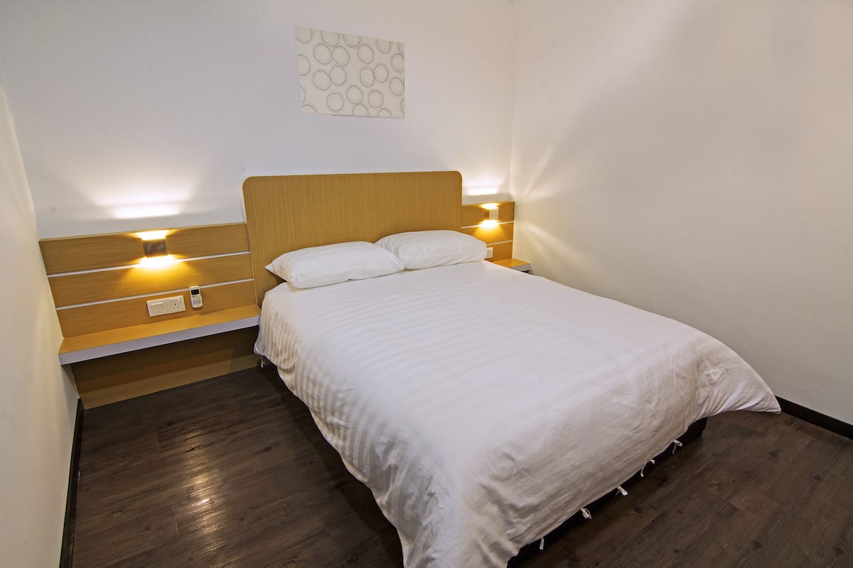 A neatly made bed with a wooden headboard, two bedside lamps, and a wall-mounted light fixture.