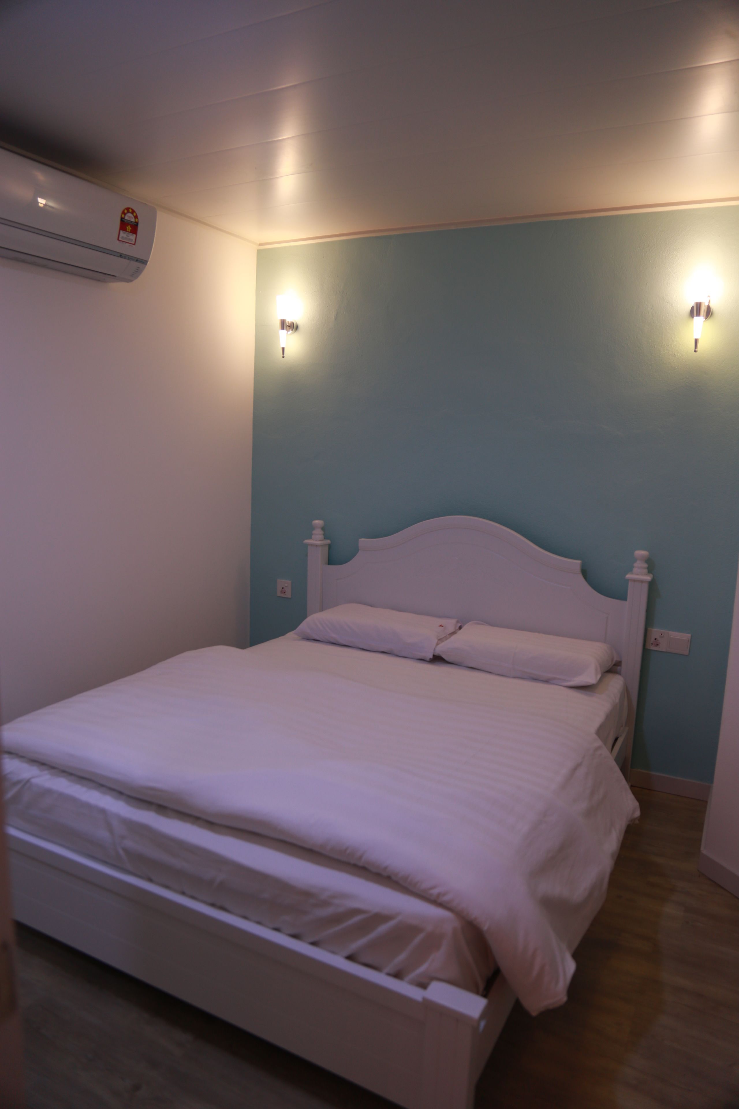 A single-bed room with a white headboard, two wall-mounted light fixtures, and an air conditioning unit on the wall.