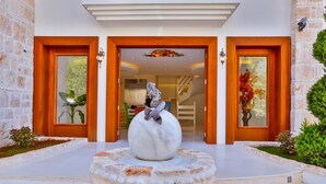 A modern building entrance with a large spherical sculpture in the center, flanked by two doors with glass panels and a staircase leading up. - Arnna Hotel (Kas)