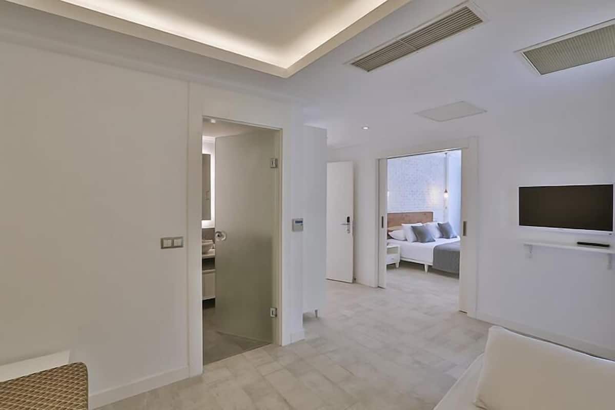 A modern hotel room with a large bed, a TV mounted on the wall, and a bathroom visible through an open door.