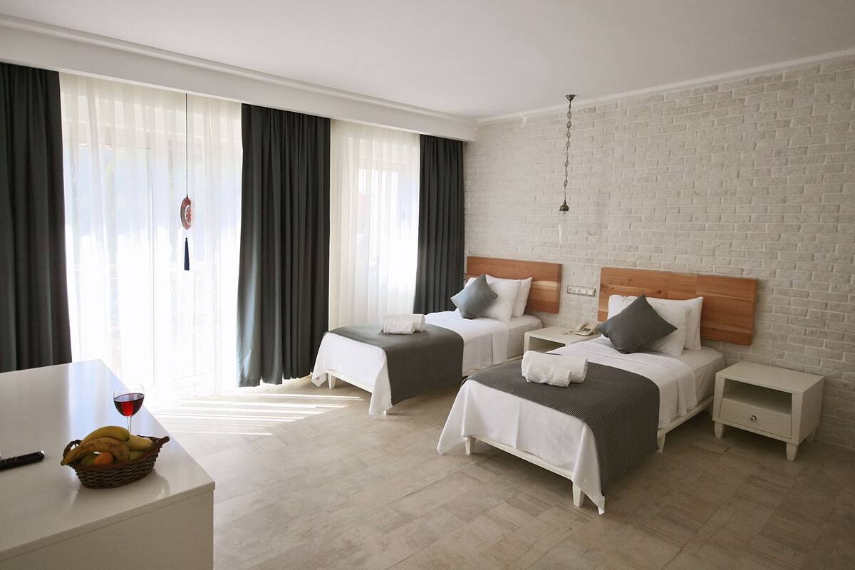 A hotel room with two beds, a desk, and a basket of fruit.