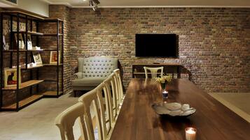 Un comedor con pared de ladrillo, un televisor de pantalla plana sobre una mesa y una estantería con diversos objetos.