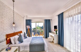 Une chambre d’hôtel moderne avec un grand lit, un bureau et un balcon agrémenté de rideaux bleus.