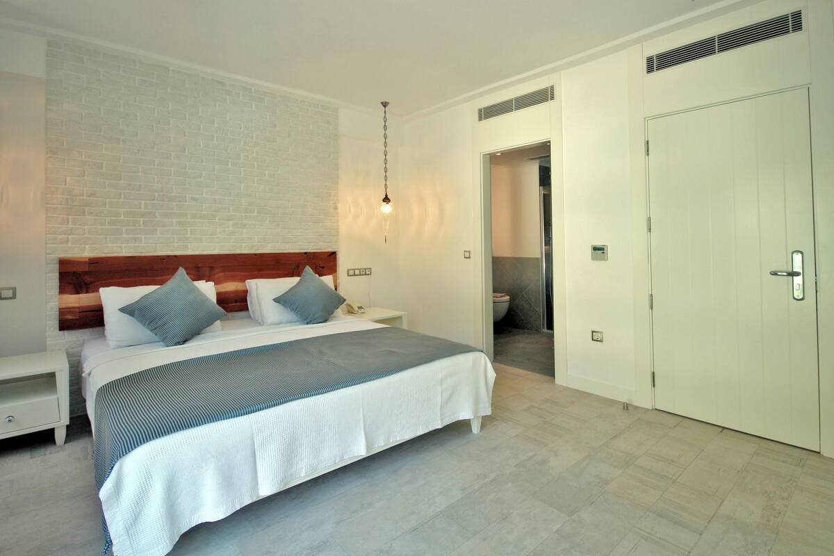 A modern bedroom with a brick accent wall, a wooden headboard, a large bed with a striped bedspread, and a white wardrobe.