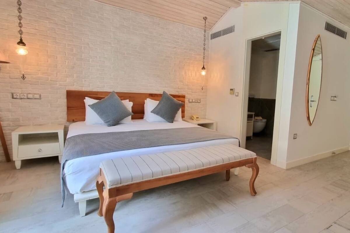 A bedroom with a bed, bedside tables, a bench, a lamp, a mirror, and a door.