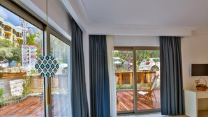 A modern living room with large windows, a sliding glass door, a flat-screen TV, and a small desk area. - Arnna Hotel (Kas)