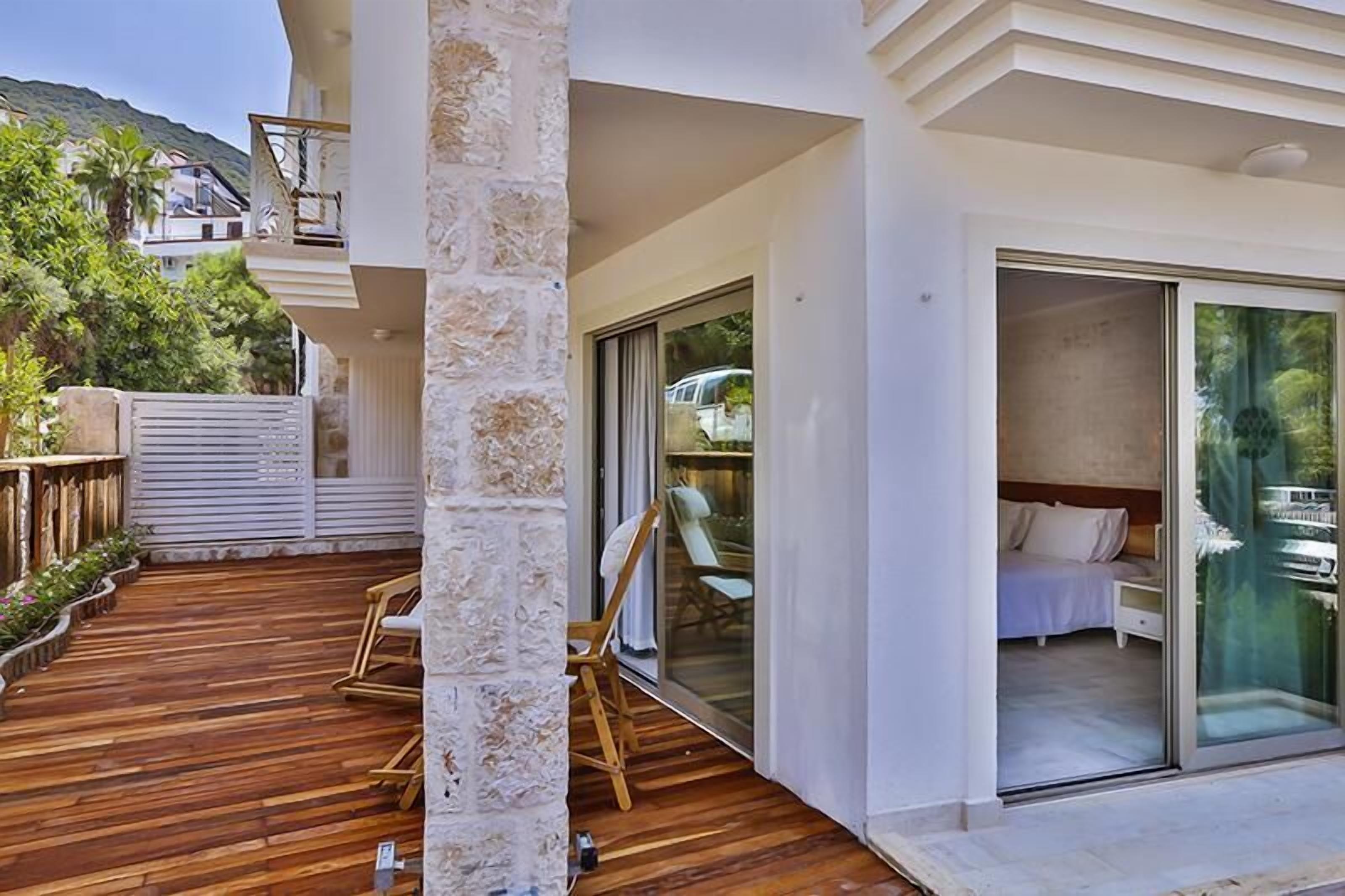 Una habitación de hotel moderna con una terraza de madera, una puerta de cristal que da a un balcón y vistas del paisaje circundante.