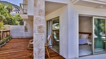 Una habitación de hotel moderna con una terraza de madera, una puerta de cristal que da a un balcón y vistas del paisaje circundante.