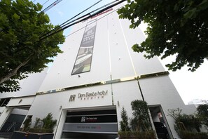 The exterior of the Den Bastian Hotel, featuring a modern design with a large vertical banner advertising the Grand Open. - Denbasta Premium Hotel Bumil (Busan)