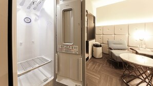 Habitación de hotel con lavadora y secadora integradas, una kitchenette pequeña, una zona de estar con una mesa redonda y sillas, y un ventanal grande.