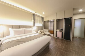 A modern hotel room with a large bed, a seating area, a vanity, and a separate toilet.