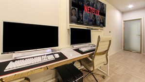 Una oficina moderna con dos monitores grandes, un escritorio con teclado y ratón, una silla y un televisor de pared que muestra contenido de Netflix.