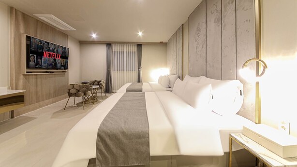 Una habitación de hotel moderna con una cama grande, un televisor montado en la pared, un escritorio y una mesita de noche.