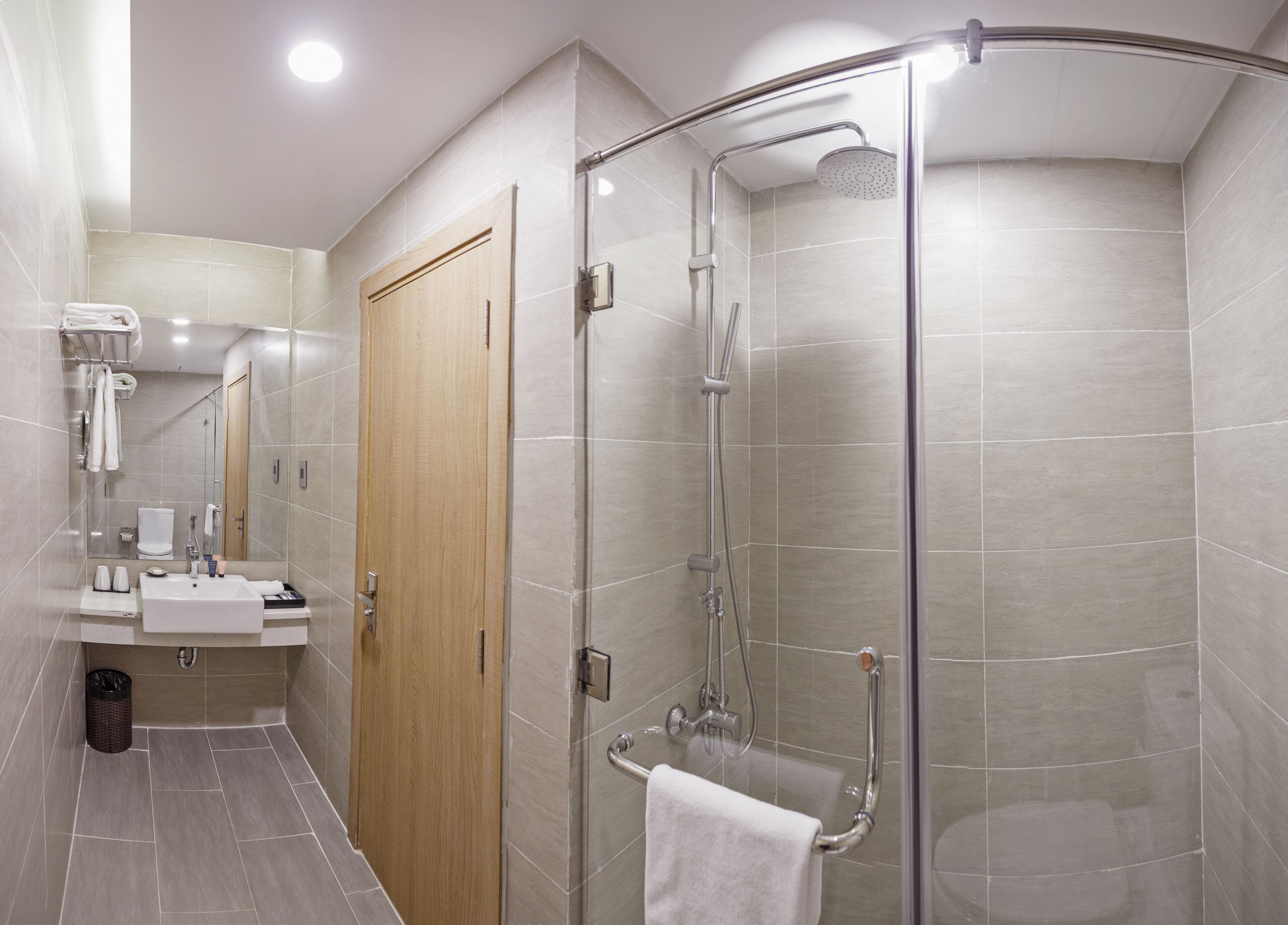 Une salle de bain moderne avec une douche à parois de verre, une porte en bois et un meuble-lavabo doté d’un évier et d’un miroir.