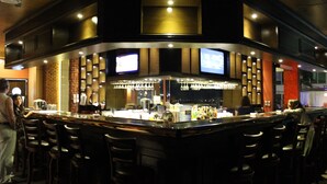 Een bar met meerdere krukken, een toonbank met barbenodigdheden en een televisiescherm.