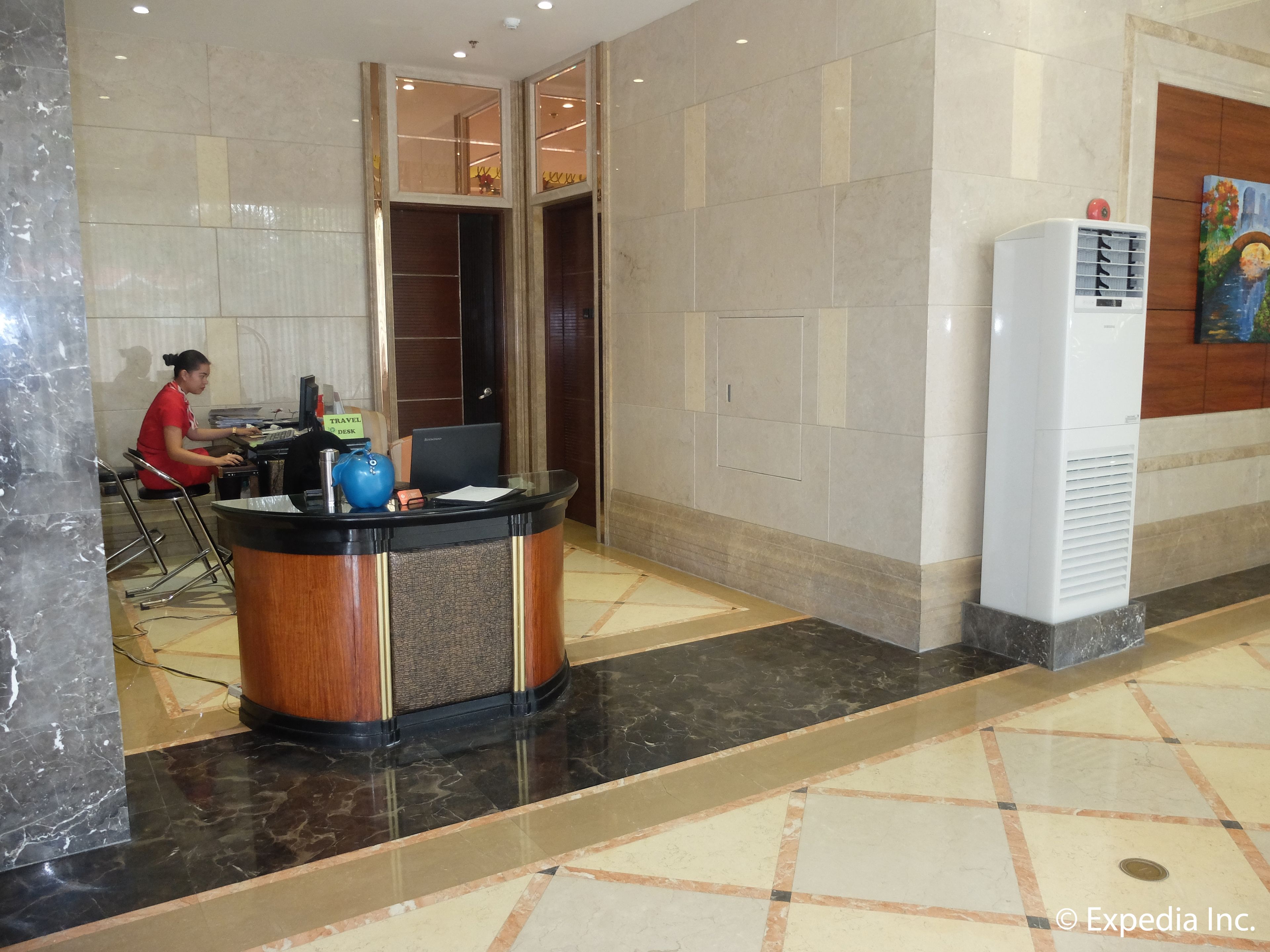 A reception desk with a computer, a travel desk sign, and a wall-mounted air conditioner.