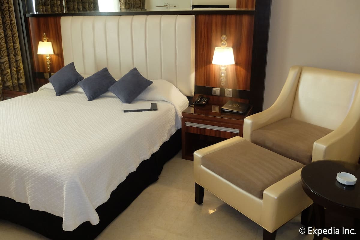 Ein Hotelzimmer mit einem Bett, Nachttischlampen, einem Nachttisch, einem Stuhl und einem kleinen Tisch.
