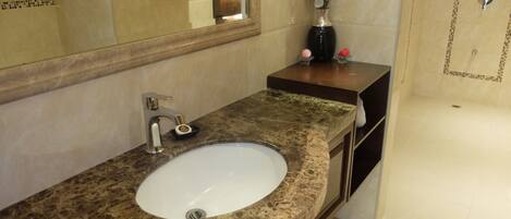 Une salle de bain avec un lavabo en marbre, un miroir et un vase contenant des fleurs blanches.