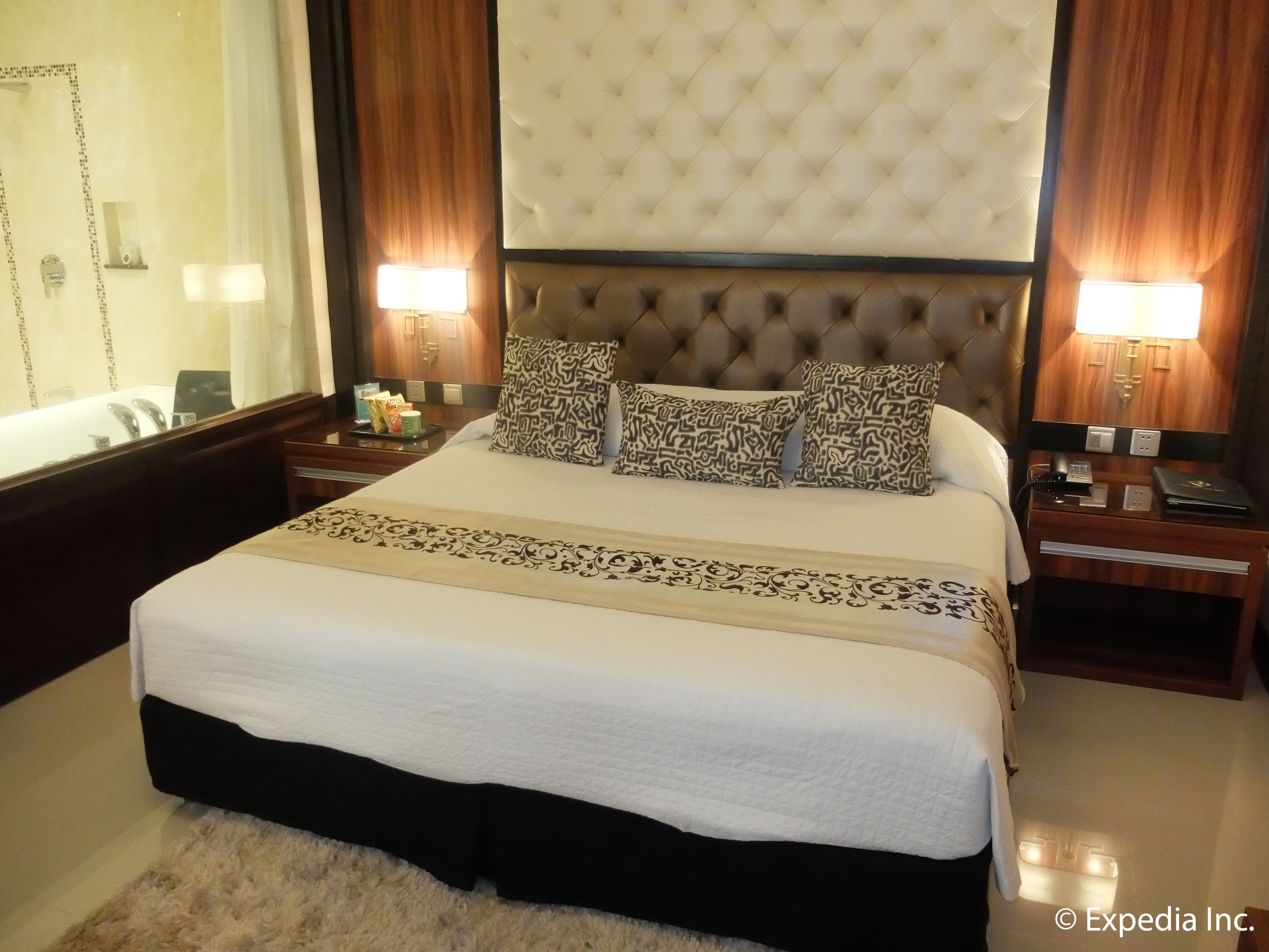 A well-appointed hotel room with a large bed, tufted headboard, decorative pillows, bedside tables with lamps, and a mirror.