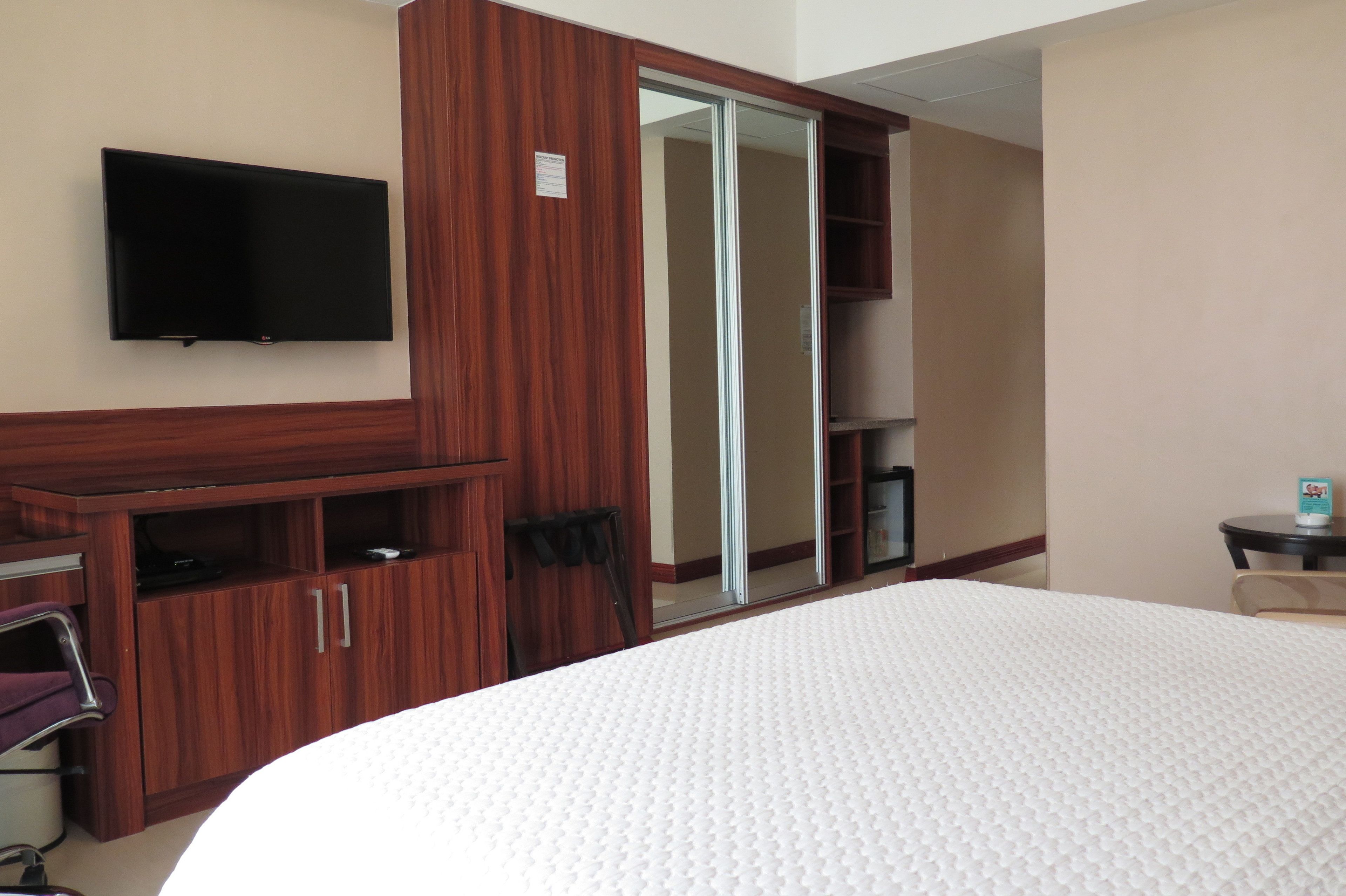 A hotel room with a large bed, a wooden wardrobe, a television mounted on the wall, and a sliding door closet.
