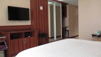 A hotel room with a large bed, a wooden wardrobe, a television mounted on the wall, and a sliding door closet.