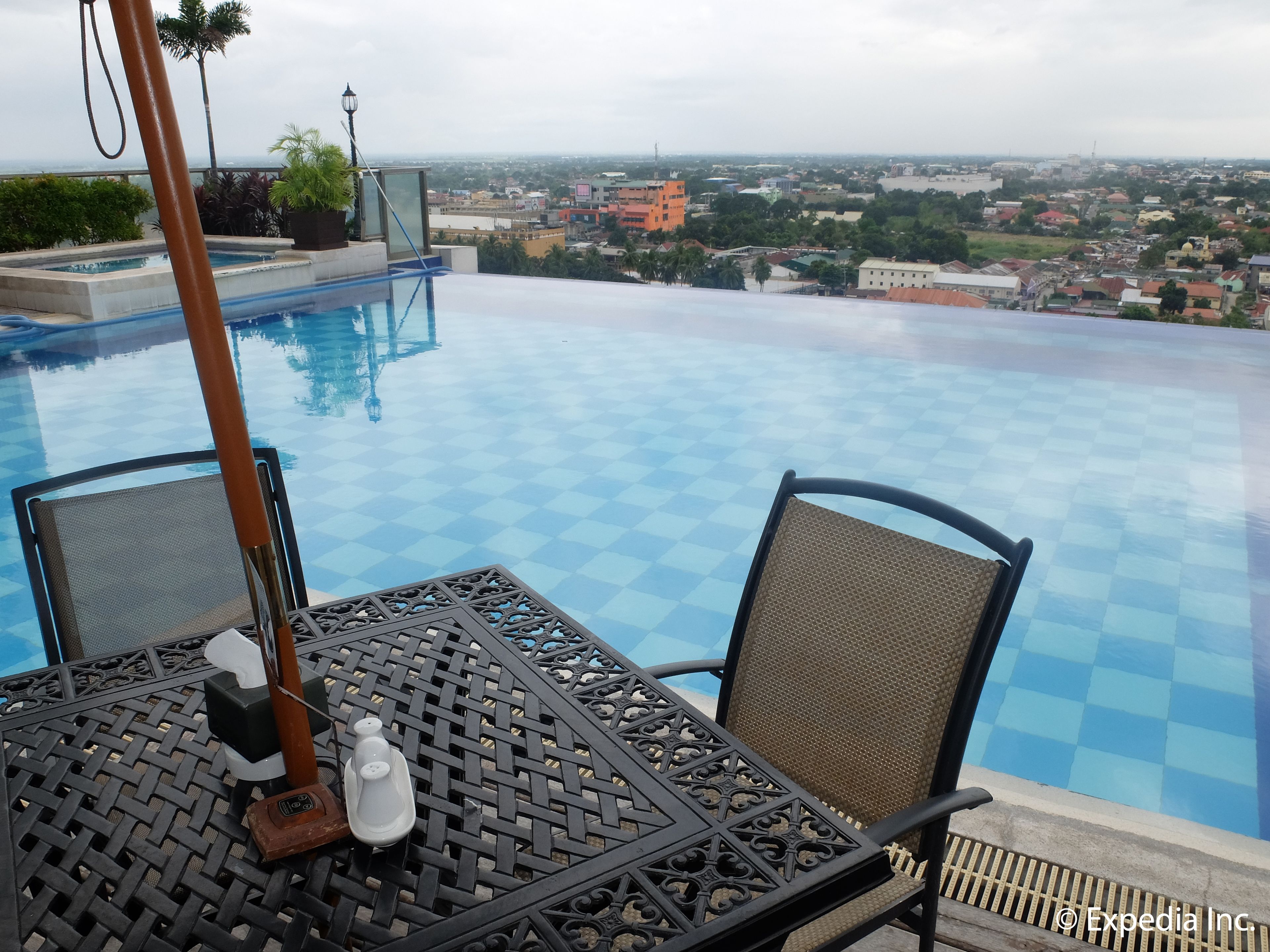 An infinity pool with a checkered pattern, two chairs, a table, and a view of a cityscape.