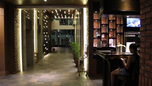 Een hotellobby met een zwart-wit schaakbordvloer, een receptiebalie, een televisie en een bar.