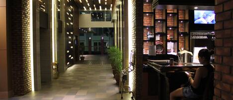 Een hotellobby met een zwart-wit schaakbordvloer, een receptiebalie, een televisie en een bar.