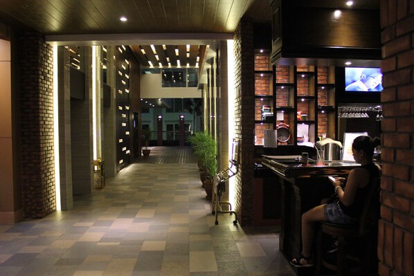 A hotel lobby with a checkered floor, a reception desk, a television, and a bar area.