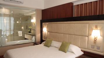 A hotel room with a large bed, a glass shower enclosure, and a wooden headboard.
