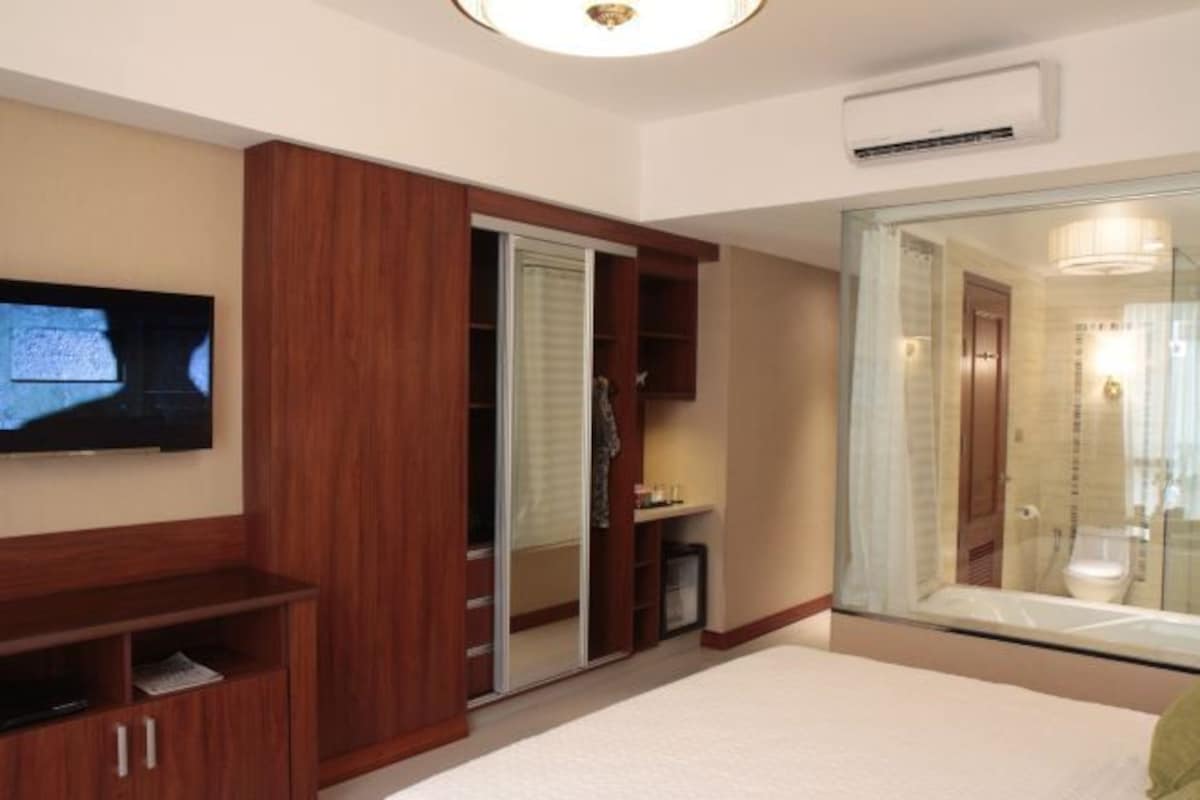 Een hotelkamer met een televisie, een houten garderobe en een douchecabine van glas.