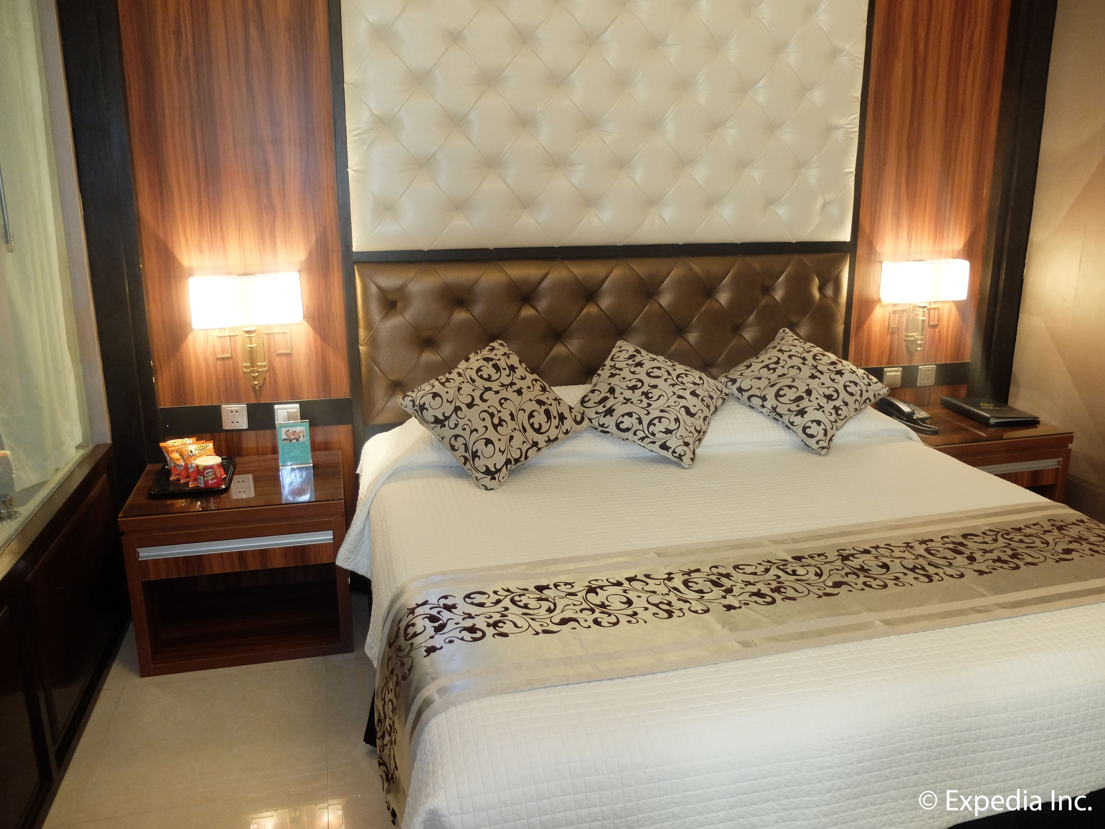 A hotel room with a tufted headboard, a large bed with patterned pillows, bedside tables with lamps, and a nightstand with a lamp and a phone.