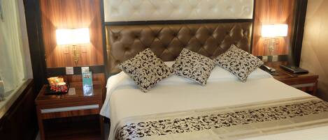 A hotel room with a tufted headboard, a large bed with patterned pillows, bedside tables with lamps, and a nightstand with a lamp and a phone.