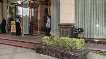 A hotel entrance with a glass door, a 'No Parking' sign, and a marble planter with greenery.