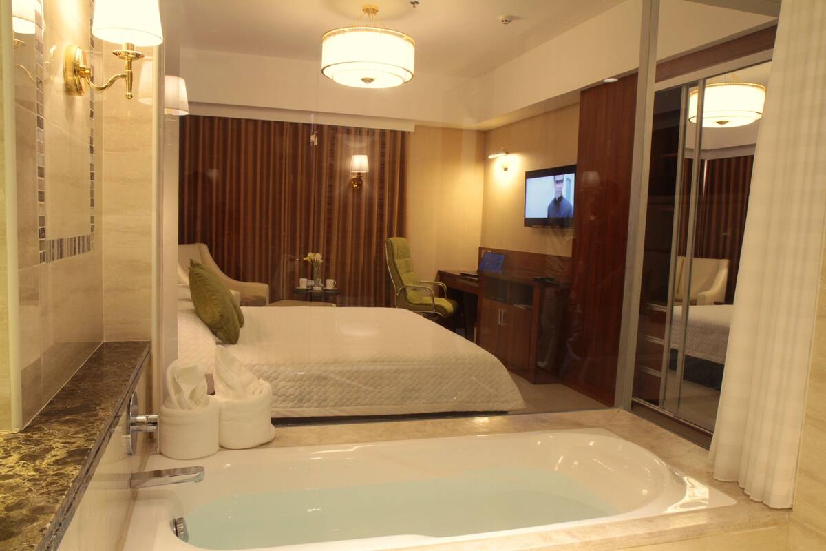 Ein modernes Hotelzimmer mit einer großen Badewanne, einem Fernseher und einem Schreibtisch mit Stuhl.