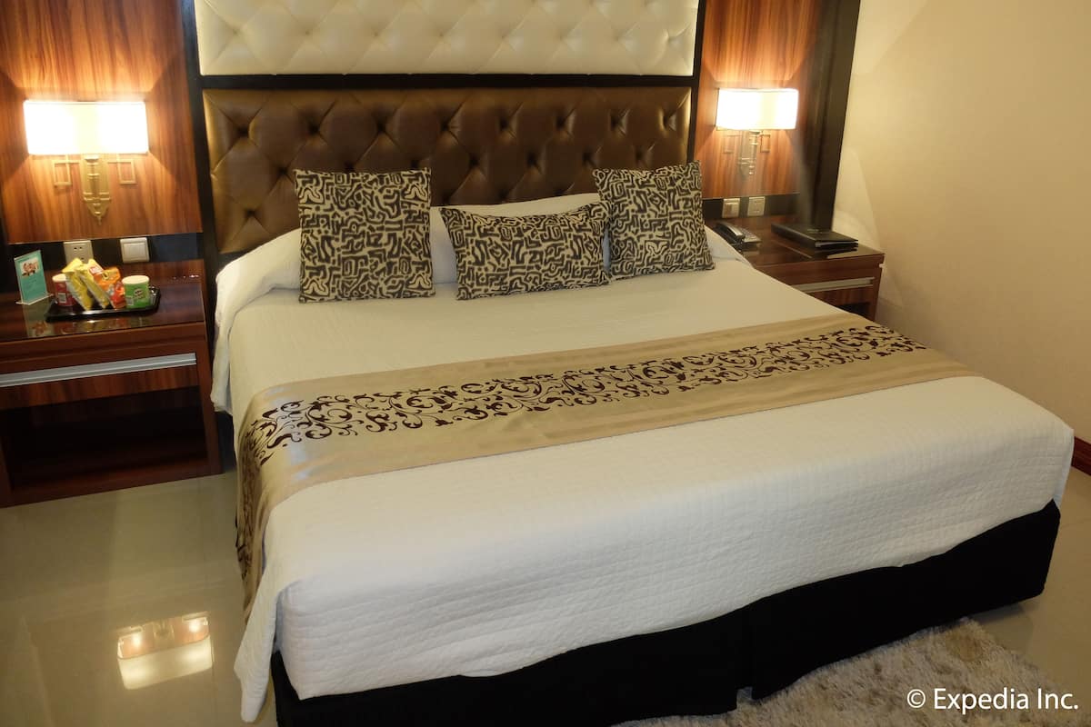 Ein Hotelzimmer mit einem großen Bett, einem gepolsterten Kopfteil, gemusterten Kissen, Nachttischlampen und einem Nachttisch mit einer Auswahl an Snacks.