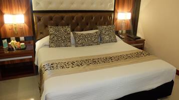 Une chambre d’hôtel avec un grand lit, une tête de lit capitonnée, des coussins à motifs, des lampes de chevet et une table de chevet sur laquelle se trouve un plateau de collations.