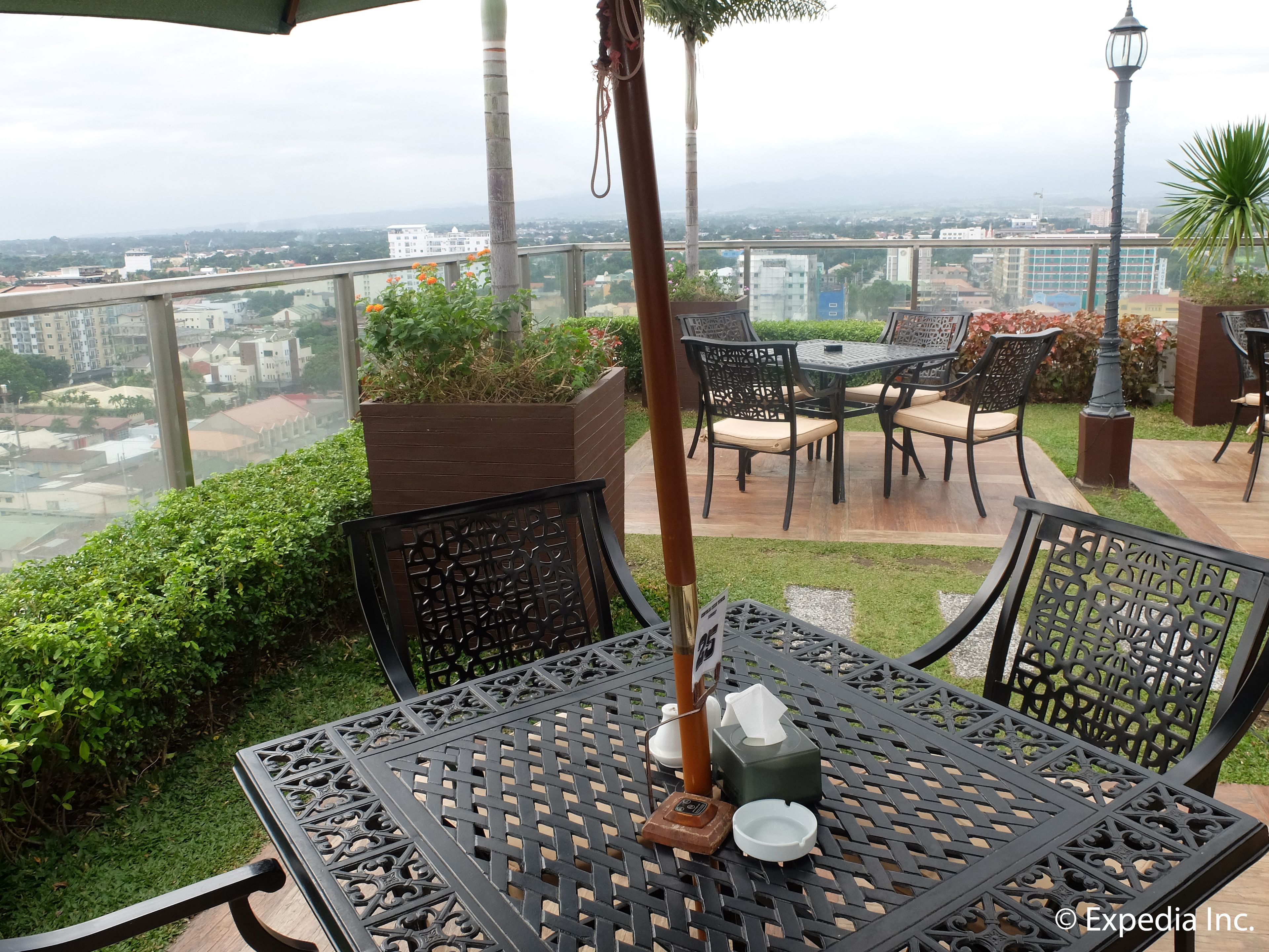 Um pátio externo com mesa e cadeiras, um vaso com flores e vista para o horizonte urbano.